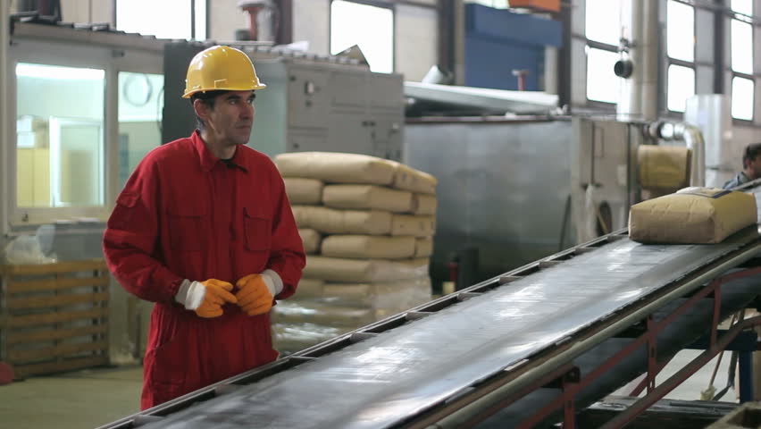 Warehouse worker in red overalls standing near a conveyor belt. HD 1080i. 