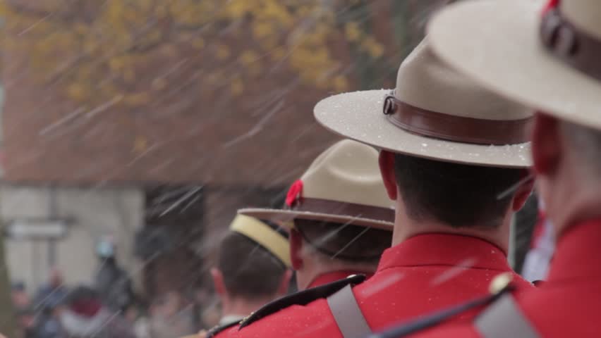 A dolly shot of a line of Canadian Police in dress uniform as they stand at attention at a ceremony on a beautiful snowy day.