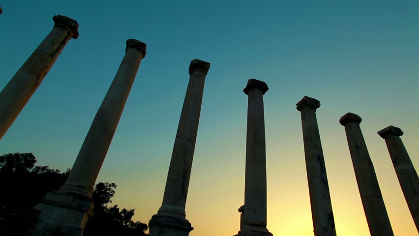 Slider dolly move left to right; the sunset makes a near silhouette of seven columns at Beit She'an, Israel.  The sky is a beautiful blend of colors.