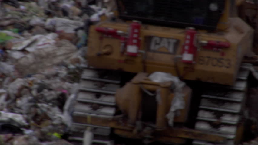 Bulldozer climbs over mounds of trash