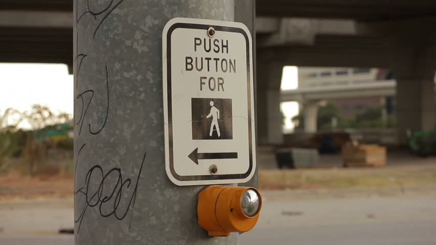 White and black pedestrian crossing sign above yellow pedestrain button on pole
