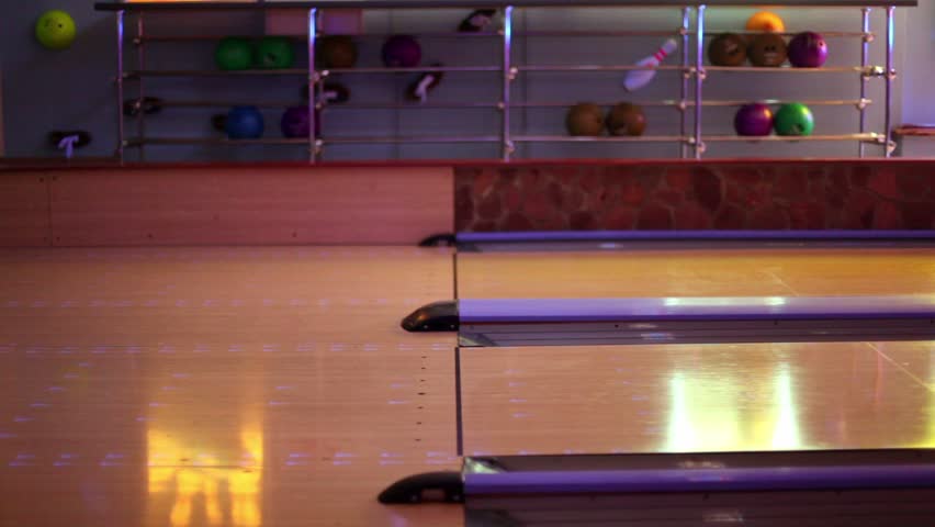 Two men throw bowling ball one by one on parallel lanes in club, only legs are visible