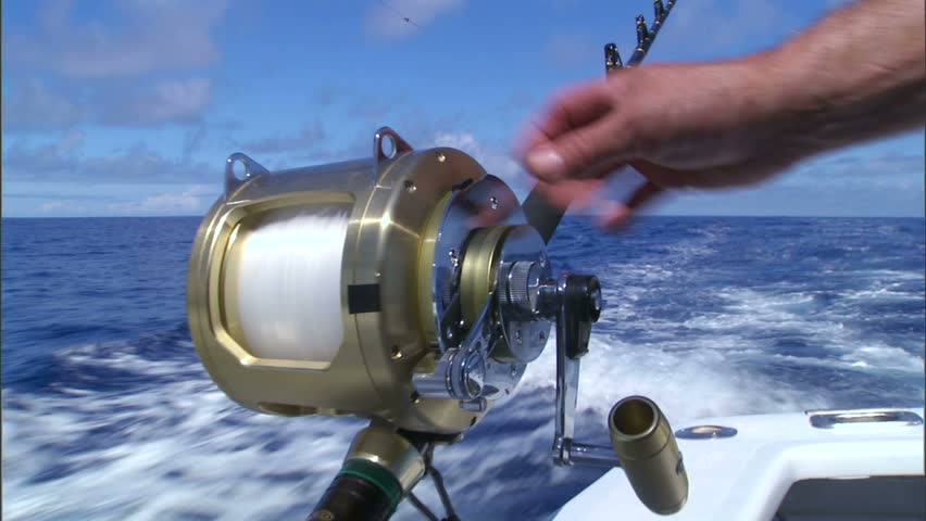 A sportfishing reel being wound by hand