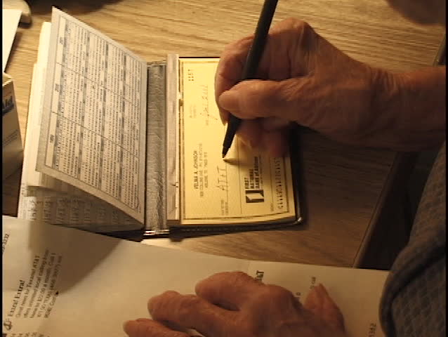 A senior citizen writes a check to pay a bill.