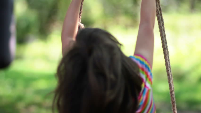 Young little girl spinning in a tree swing and smiling
