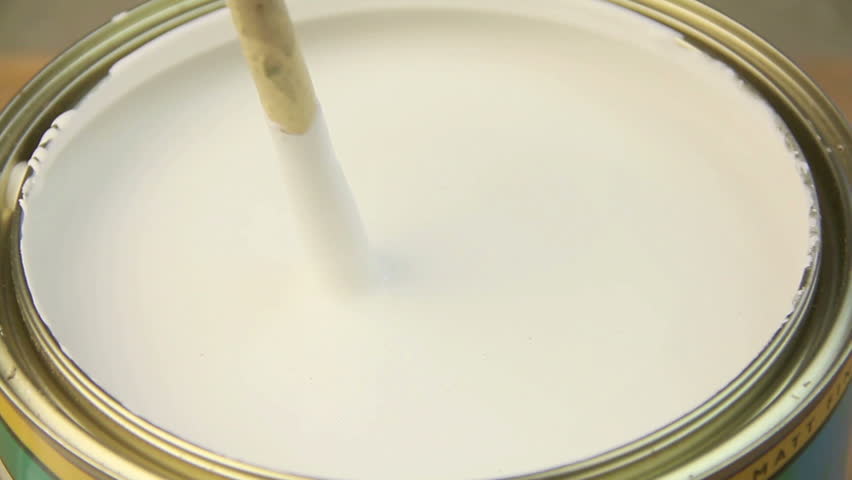 Mixing and stirring white paint in a tin with a wooden spoon.