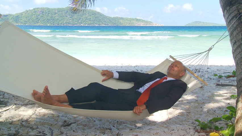 elderly manager relaxing in hammock under palmtrees on the beach