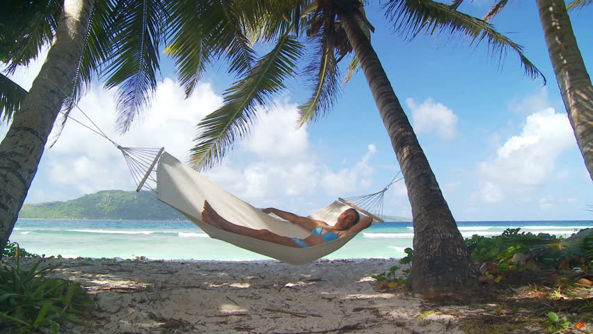young woman in bikini enjoying her nap in hammock in the shade of palmtrees on tropical beach