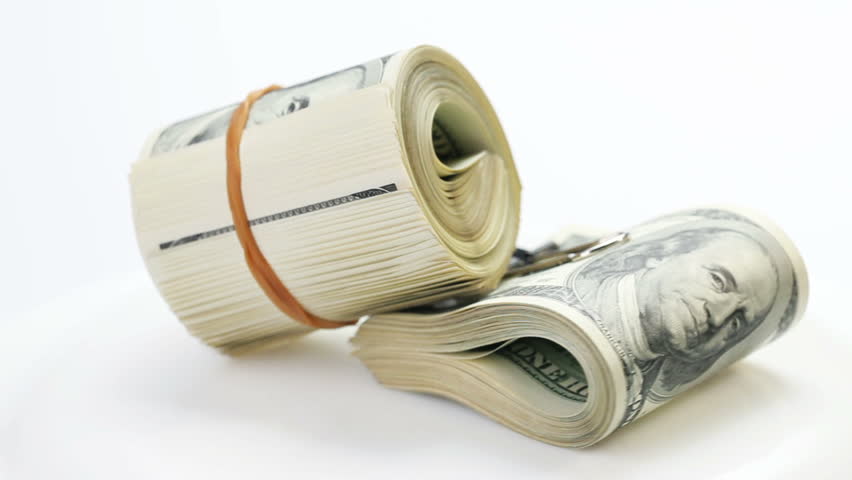 Bundle of many 100 dollar bank notes rolled up and fasten with paper clip rotating on a white background