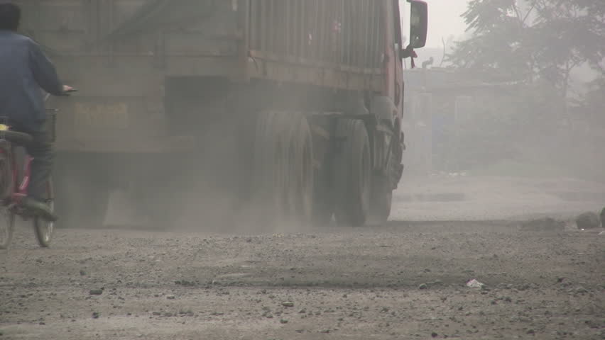 =A worker rides his bike behind a truck at a dusty street in Qingdao