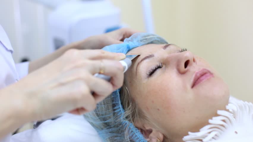 Woman-cosmetician does ultrasound peeling on face for woman closeup