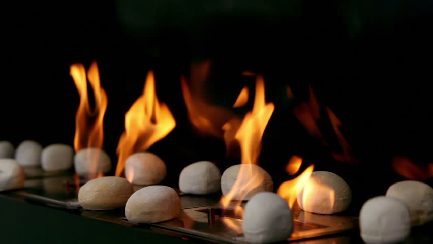 Tongues of flame go through slot in metal plate with round stones on it