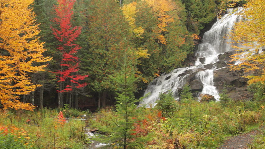Locked down view of colorful fall foliage surrounding a large, lovely waterfall in New Hampshire. 