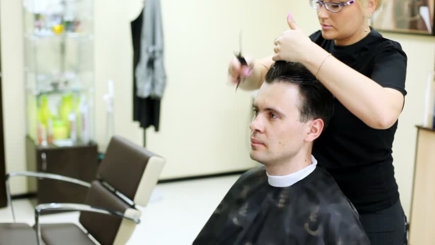 Hairdresser cuts hair to man to brunet with long hair by scissors