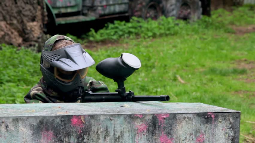 Boy paintball player sits in ambush behind metal fence