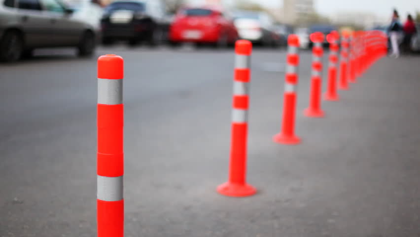 protective barrier made of red striped columns, people and cars go road, focus on first column