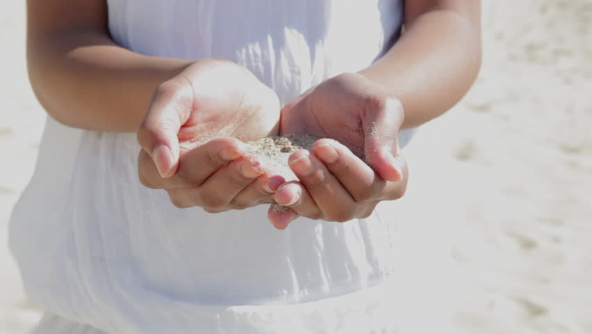 Close up view of a girl's hands with white sand filtering through her fingers while standing on a beach.