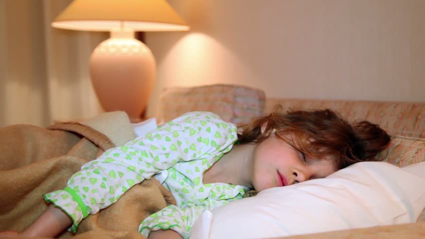Little girl wakes and smile in bed at background of lamp