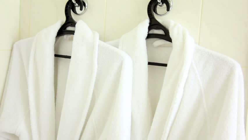 Two soft white bathrobes hang on hanger, downward motion