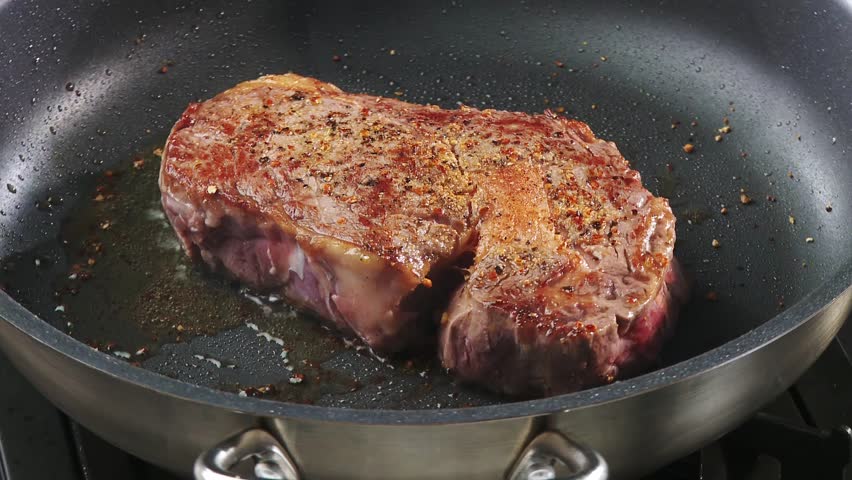 Frying rib eye steak in a frying pan