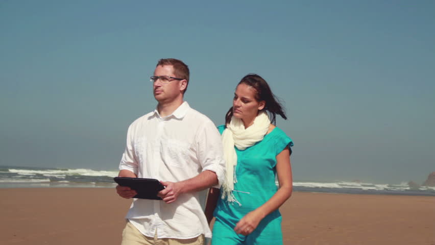 Young couple with tablet computer sightseeing the beach,  camera stabilizer shot 
