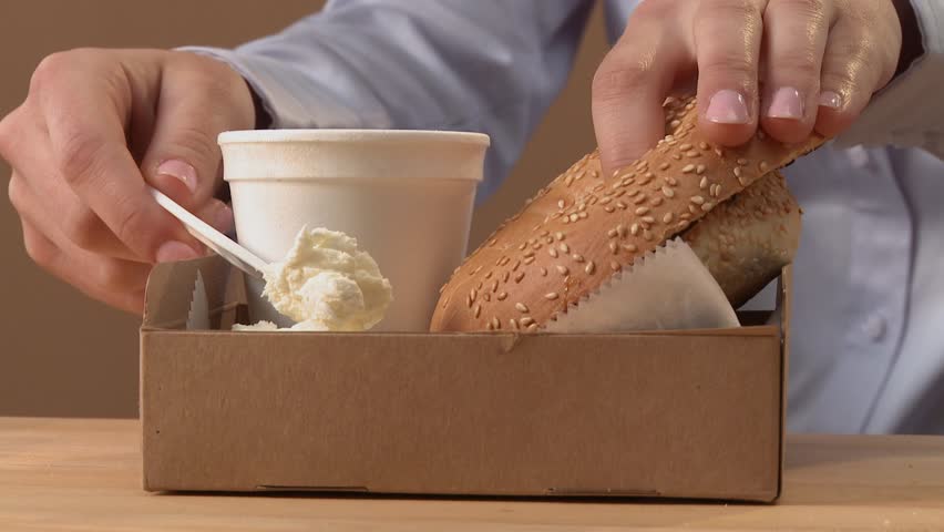 Young woman biting into half a bagel spread with cream cheese