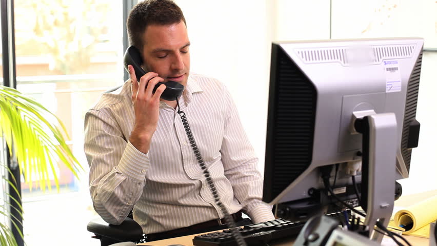 Business male talking on phone in office and looking at computer screen