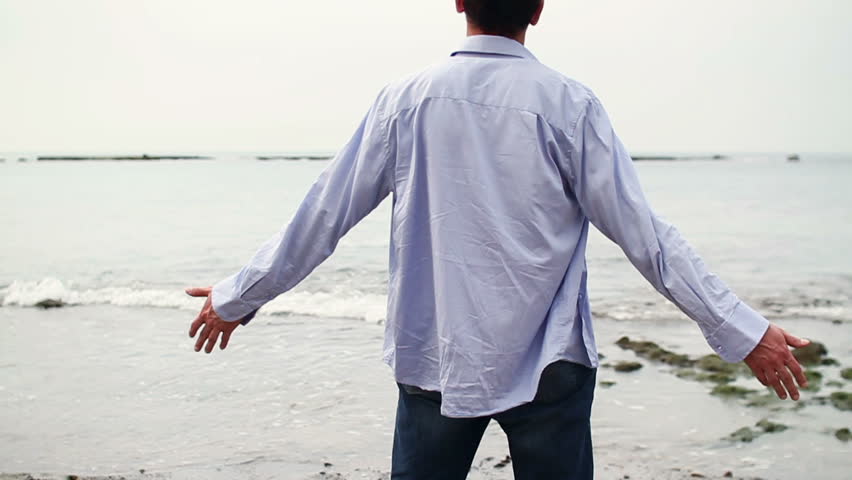 Man with wide open arms standing on the beach, steadicam shot
