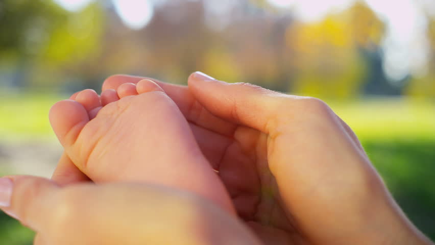 Portrait in close up of a mothers hands cradling the foot of her baby