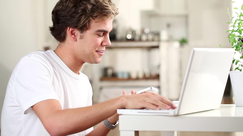 Attractive young student using laptop and mobile phone at home