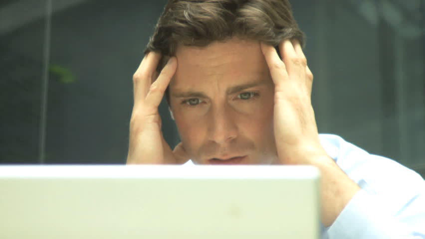 CLOSE UP MALE LOOKING STRESSED AT LAPTOP