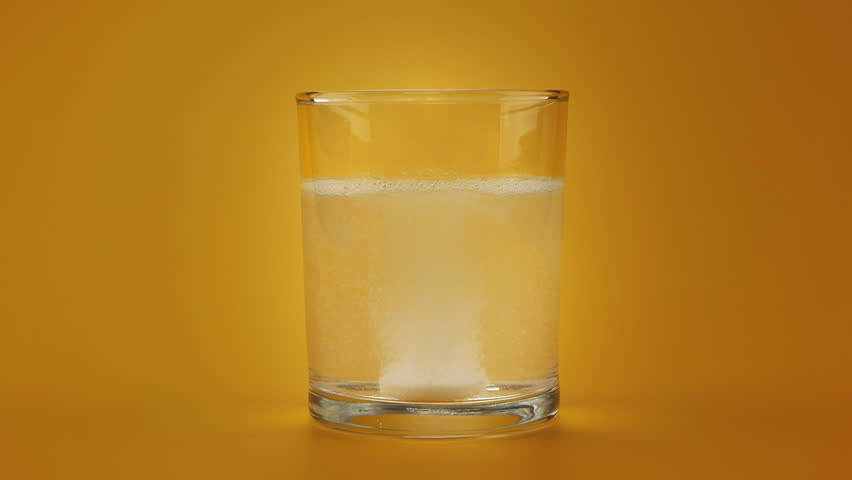 Aspirin or effervescent pill dropping into a glass of water and dissolving