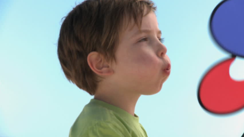 MEDIUM CLOSE UP OF A BOY BLOWING ON A PIN WHEEL