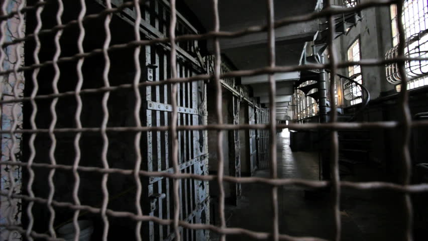 Camera pan through grilled bars to prison cells
