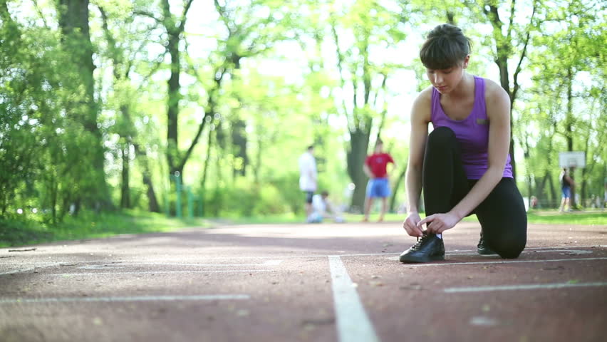 Young woman tying running shoes before run, dolly shot
