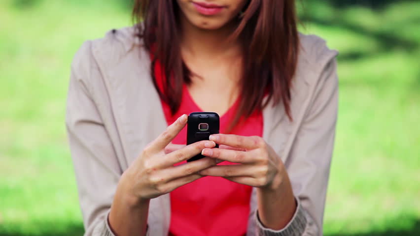 Serious brunette woman texting on her mobile phone in a parkland