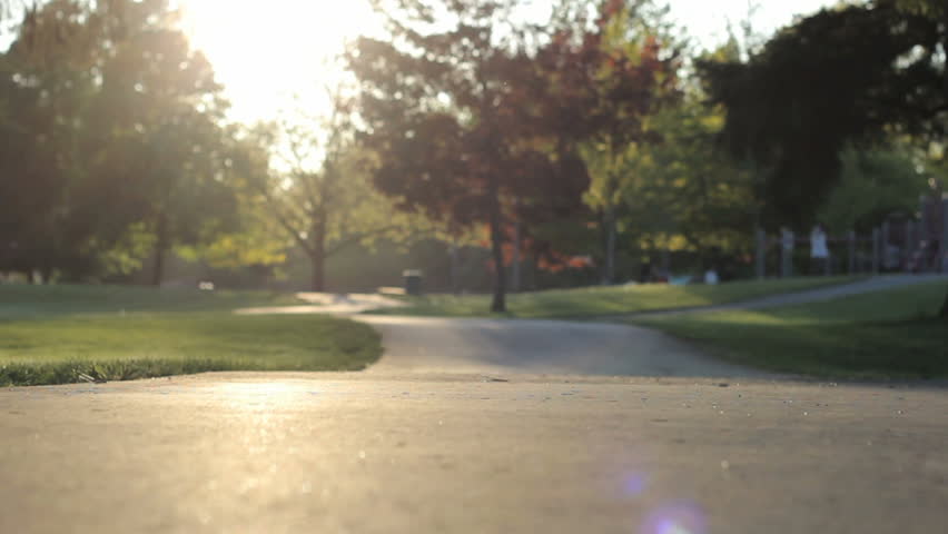 A cute little Asian girl slowly rides her pink bike with streamers and training wheels to the playground into the sunset.