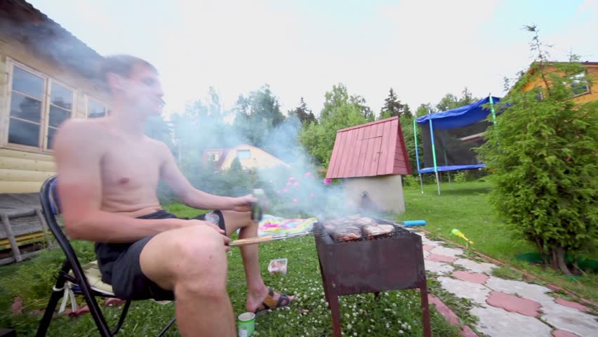 Man sit in smoke and makes kebab on grill near country house, around motion