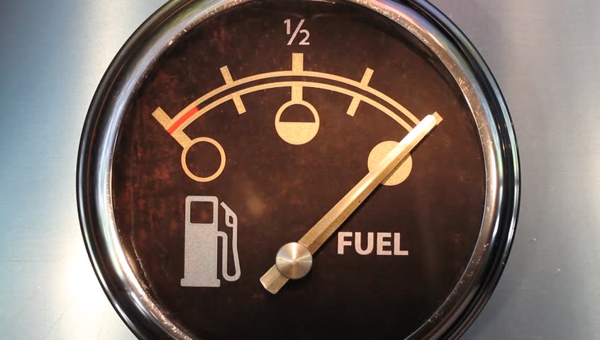 Simulated time lapse of vehicle fuel gauge moving to empty before refueling with moving background visible in reflections.
