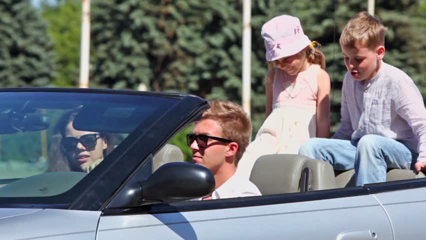 Young couple with two kids ride backward in cabriolet at sunny summer day