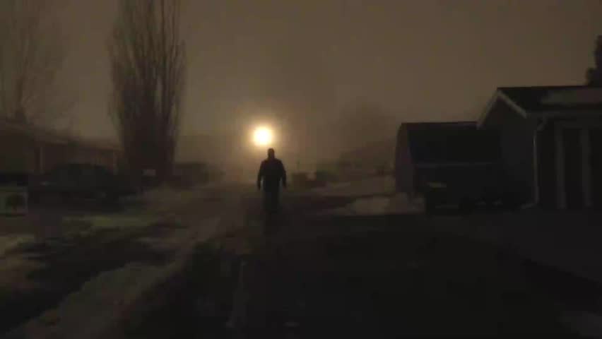 Unidentifiable actor, dark dressed man, approaching camera slow and steady in eerie fog, set at night, and in a narrow alley.