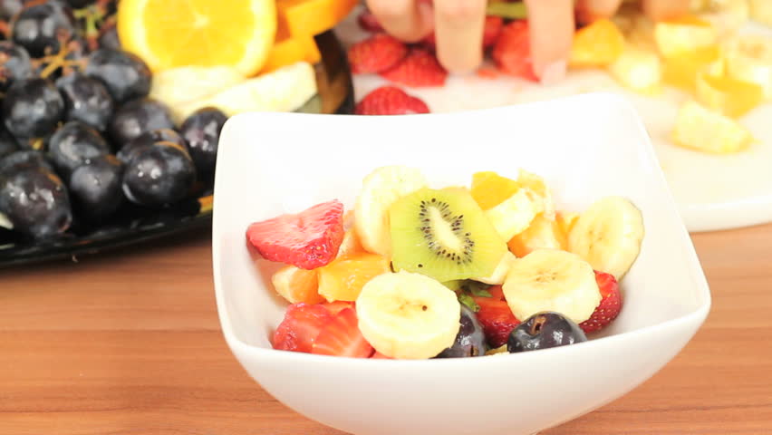 Tasty fruit salad in the making - strawberries, grape, orange kiwi and banana slices mixed in a white bowl