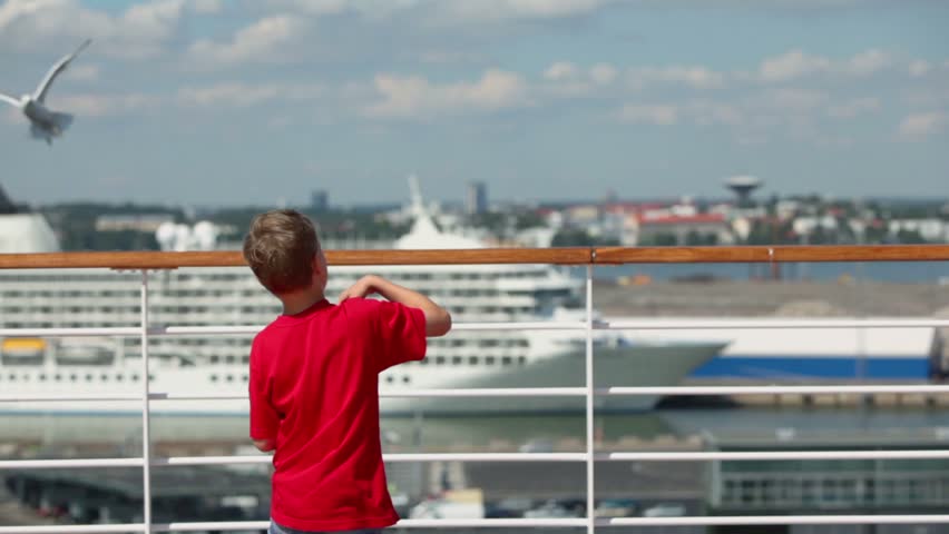 Little boy throws pieces of bread to feed gulls in port at sunny day