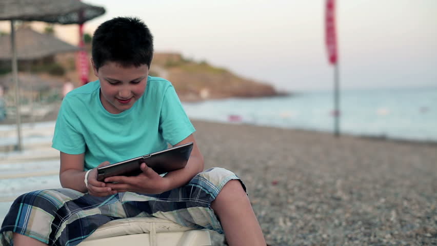 Happy boy playing with tablet computer on the beach
