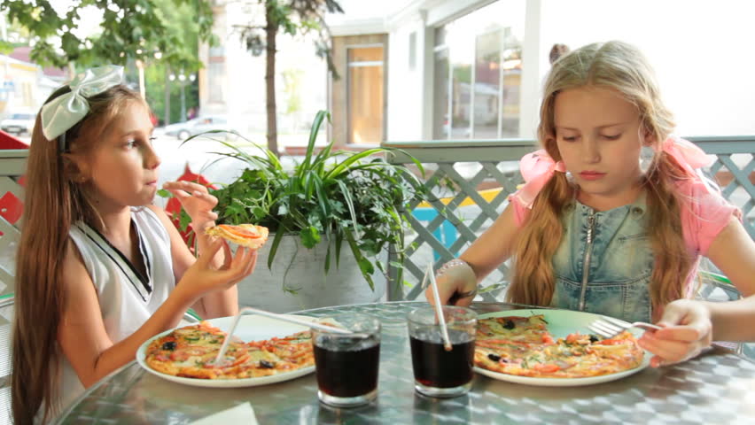 Two little girls eating pizza in a fast food restaurant outdoors