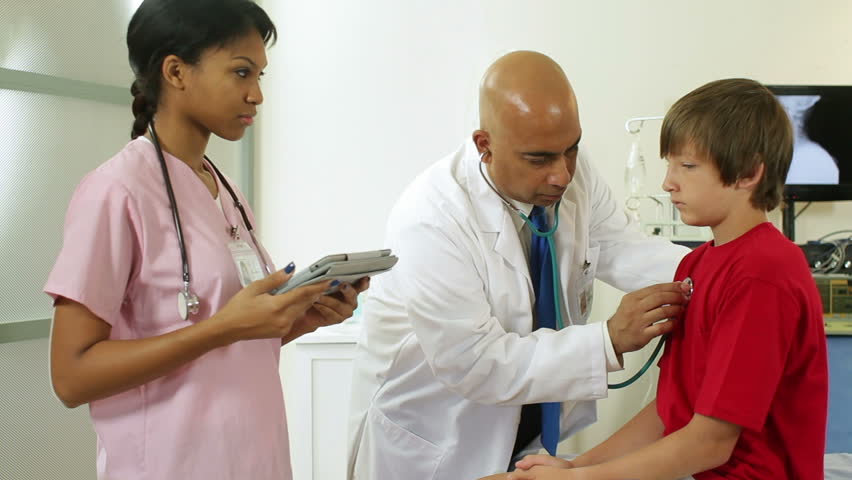 Indian pediatrician finishes exam and instructs pretty African American nurse about patient care for boy.