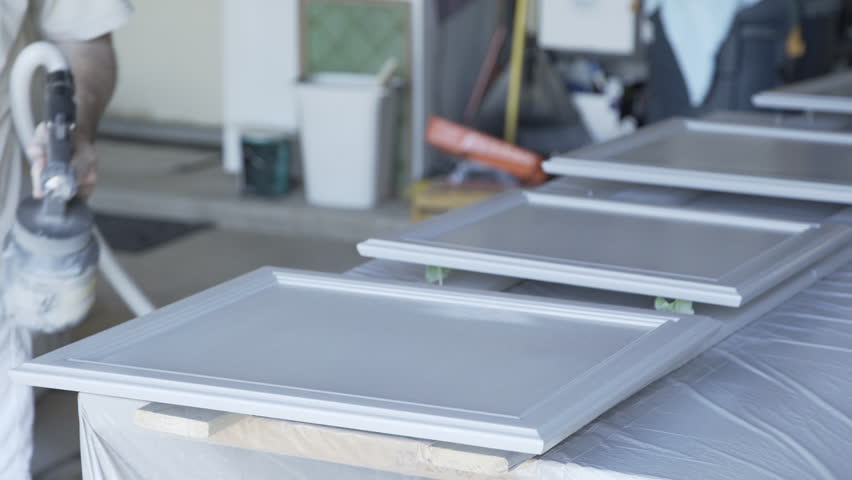 A Homeowner Handyman Type In His Garage Using Paint Sprayer To A Homeowner Handyman Type In His Garage Using Paint Sprayer To Cabinet Doors
