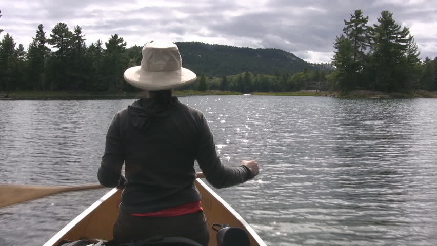 Woman paddles canoe on sunny water. POV. North Ontario, Canada.