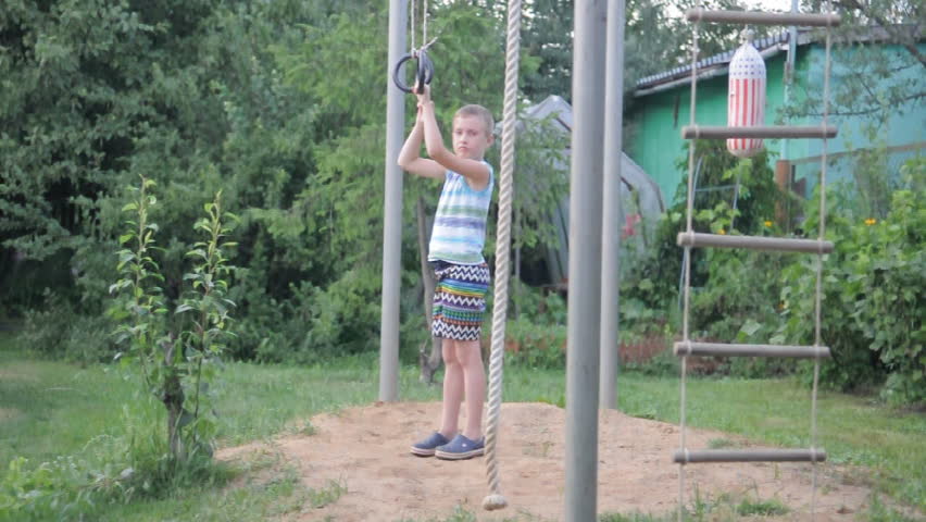 young funny boy exercising on gymnastic rings and laughing