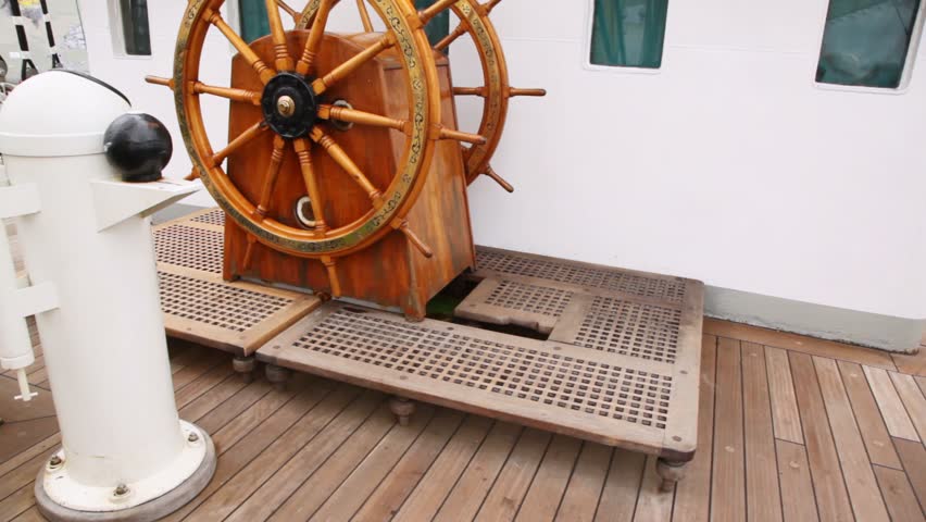 Old steering wheel from wood stands on sailing vessel deck Krusenstern against captain cabin
